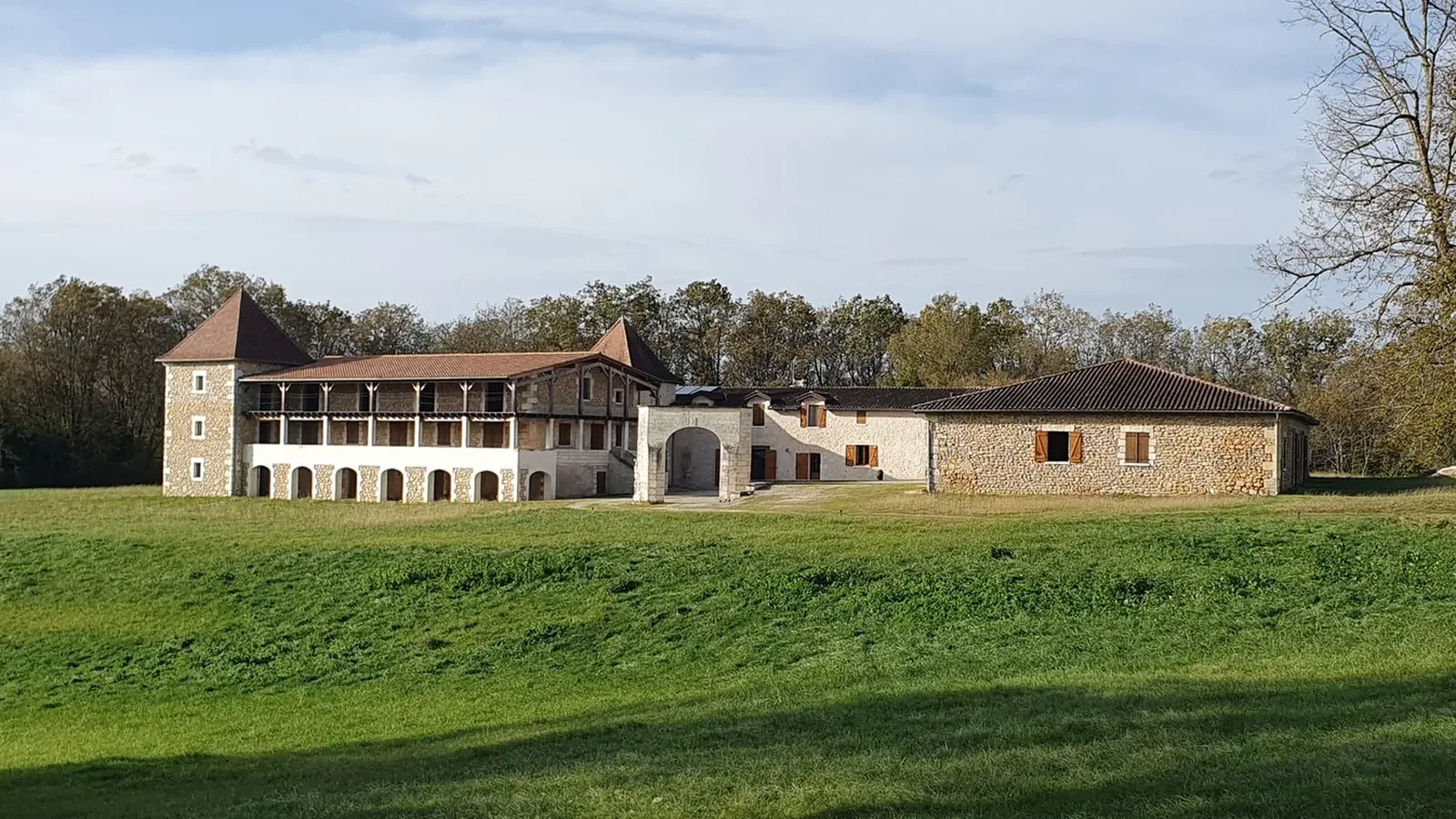 Maison de pierre à deux tours coiffées de tuiles et à loggia couverte, au bout d'une prairie, à Bourdeilles